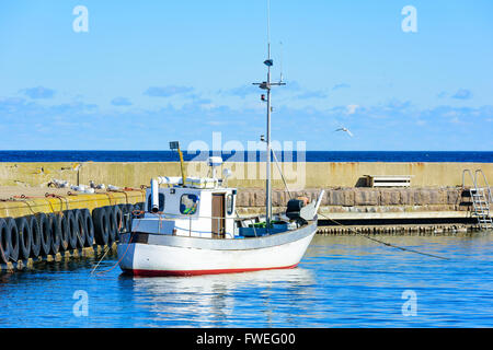 Small white fishing boat moored by the stone pier in the harbor. Gulls sit beside it on the pier. Fine, sunny weather and very l Stock Photo