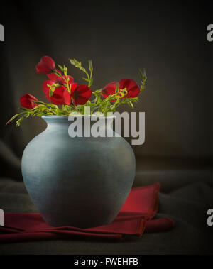 Still life of red wild flowers in a Roman style blue stone textured vase Stock Photo