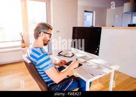 Man sitting at desk working from home on computer Stock Photo