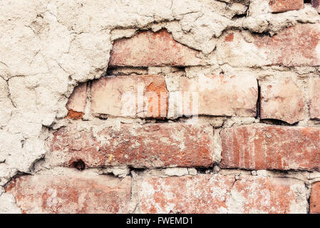 Old weathered brick wall fragment with pieces of plaster. Stock Photo