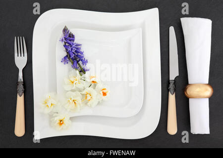 Elegant place setting with white porcelain dishes, antique cutlery, spring bluebell and narcissus flowers with napkin and ring. Stock Photo