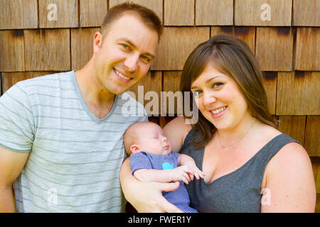 An attractive couple holds their newborn baby in their arms. Stock Photo