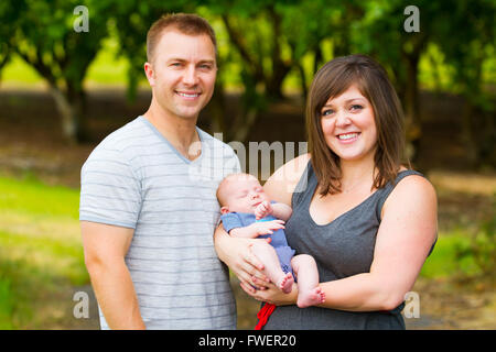 An attractive couple holds their newborn baby in their arms. Stock Photo