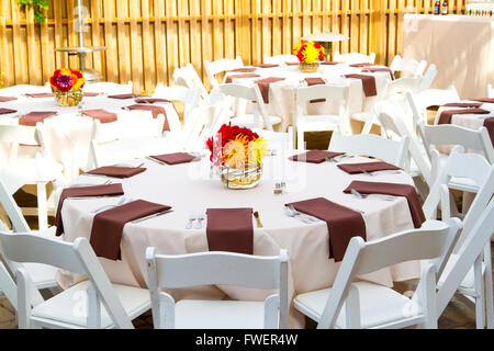 Place settings, tables, and chairs are empty before the guests arrive at a wedding reception. Stock Photo