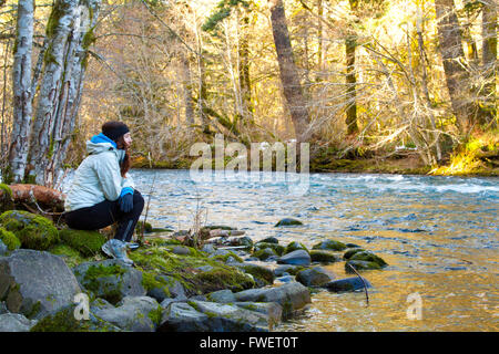 A female hiker takes a rest and looks out over the water of the McKenzie River in Oregon. Stock Photo