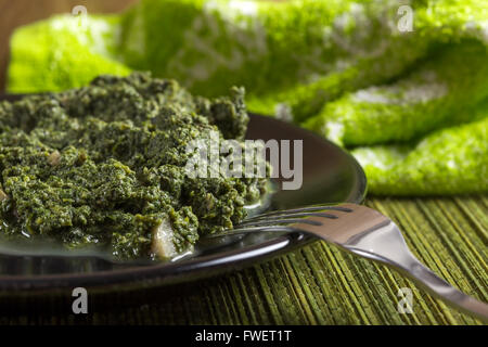 Stewed nettles with cream sauce and garlic on dark plate with fork Stock Photo