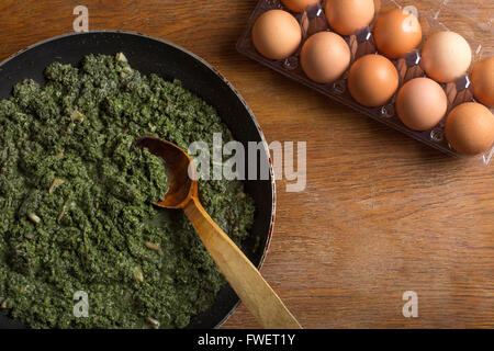 Stewed nettles with cream sauce and garlic in cooking pot with spoon on rustic background Stock Photo