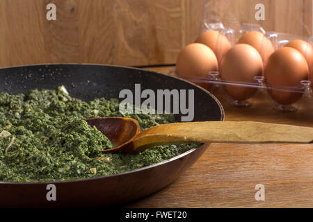 stewed nettles with cream sauce and garlic in cooking pot with spoon on rustic background Stock Photo