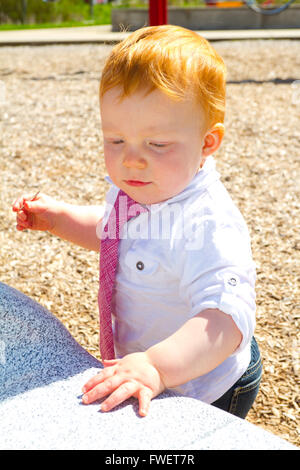A caucasian baby boy plays at the park wearing a white shirt and a tie. Stock Photo