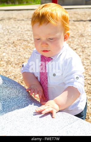 A caucasian baby boy plays at the park wearing a white shirt and a tie. Stock Photo