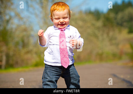 A one year old boy taking some of his first steps outdoors on a path with selective focus while wearing a nice shirt and a neckt Stock Photo