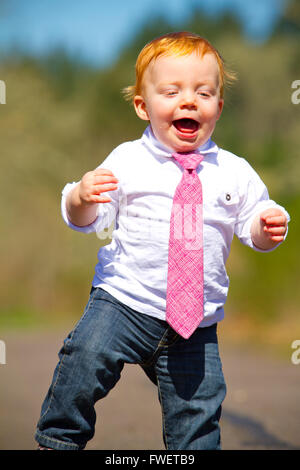 A one year old boy taking some of his first steps outdoors on a path with selective focus while wearing a nice shirt and a neckt Stock Photo