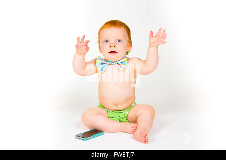 A one year old boy plays with a cell phone in the studio with a white background. Stock Photo