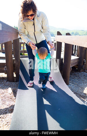A mom and her son cross an unstable bridge at a playground together. Stock Photo
