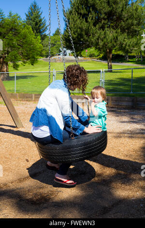 A son and his mom share a tire swing at the playground of a park in Oregon. Stock Photo