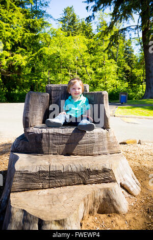 A cute young boy sits on a stump carved into a seat at a park outdoors for this cute and simple portrait. Stock Photo