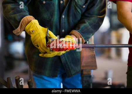 A very talented glassblower is forming and shaping glass in a studio for glass making. He is creating a fluted bowl from this pi Stock Photo