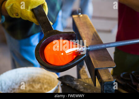 A very talented glassblower is forming and shaping glass in a studio for glass making. He is creating a fluted bowl from this pi Stock Photo