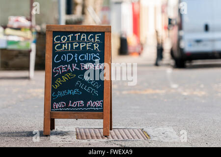 Blackboard A-frame sign outside the 'Cottage Chipper' mobile fish and chip van advertising cod, steak burgers, wraps, chicken fi Stock Photo