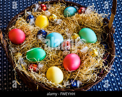 Colored Easter egss in basket with chocolates Stock Photo