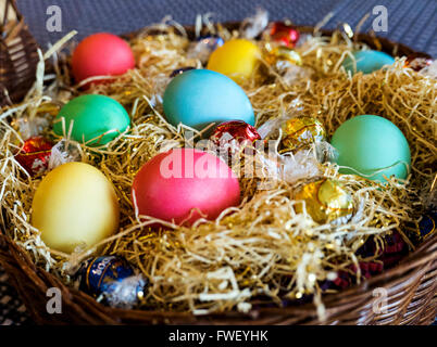 Colored Easter egss in basket with chocolates Stock Photo