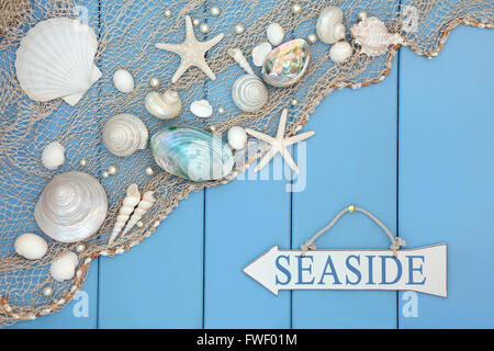 Abstract scene with seaside sign, shells, pearls and fishing net over wooden blue background. Stock Photo