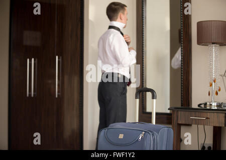 Young traveler businessman wearing white shirt standing at the mirror and getting dressed for meeting or work after arriving Stock Photo