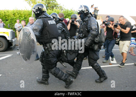 Armed police officers watch Loyalists during trouble in north Belfast after a sustained attack on police in the Woodvale area of Stock Photo