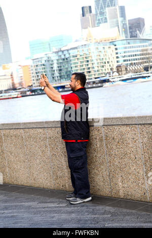 London - 5 April 2016 - Tourist takes a selfie with City Hall and Tower Bridge in the background on a sunny day in London Credit:  Dinendra Haria/Alamy Live News Stock Photo