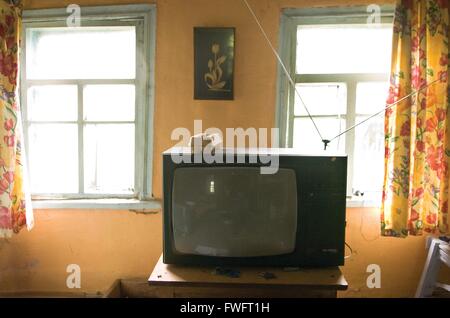 An old TV in a room of a poor family home in Ukraine. The room is pained peach, but dark and in disrepair. Stock Photo