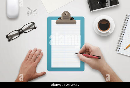 Man hand writing on notebook surrounded with office accessories. Top view of work desk. Coffee, glasses, pencil, mouse, paper Stock Photo