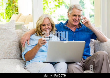 Senior couple using laptop while talking on phone at home Stock Photo