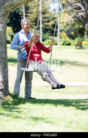 Senior man pushing his partner on swing Stock Photo