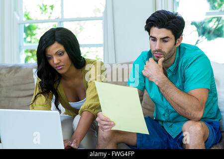 Thoughtful man checking at bills while woman using laptop Stock Photo