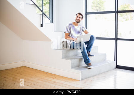 Happy man sitting on steps using laptop Stock Photo