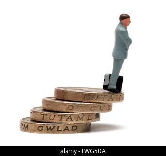 A miniature figurine businessman standing on a stack of pound coins. Stock Photo