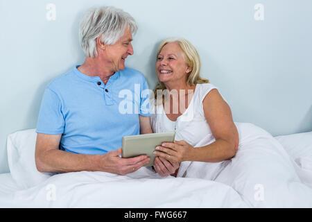 Happy senior couple using digital tablet while relaxing on bed Stock Photo
