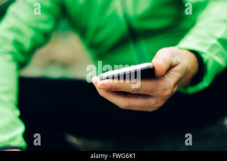 closeup of a young caucasian sportsman wearing sport clothes using his smartphone outdoors Stock Photo