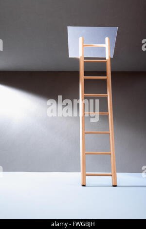 Escape concept. Wooden ladder in empty room with illuminated hatch in ceiling Stock Photo