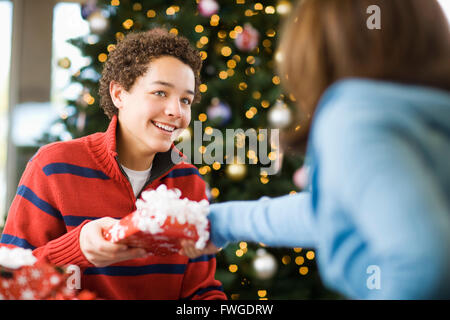 A boy and girl by a Christmas tree exchanging presents. Stock Photo