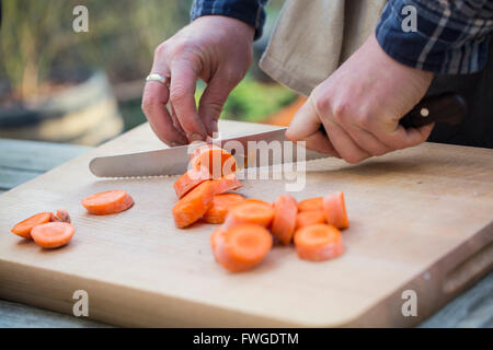 A man chopping vegetables on a board with a knife, slicing carrots. . Stock Photo