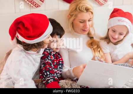 A woman and three children using a laptop computer sitting in a row in bed on Christmas morning. Stock Photo