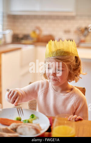 A young girl wearing a party hat, sitting at a table having a meal. Stock Photo