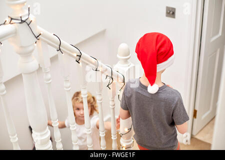 A boy and girl rushing down the stairs on Christmas morning, one wearing a Santa hat. Stock Photo