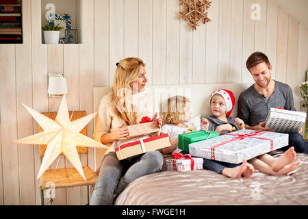 A family, two adults and two children sitting in bed on Christmas morning opening presents together. Stock Photo