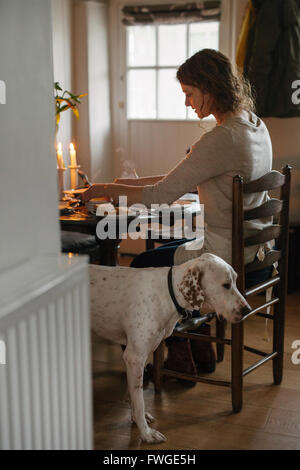 A woman seated at a table in a ladderback chair, a large white dog beside her. Stock Photo