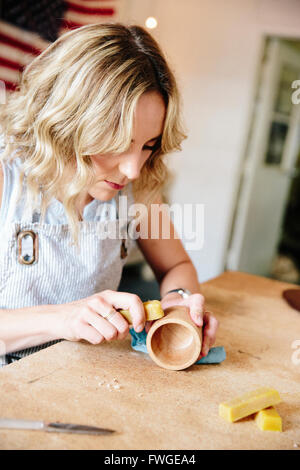 A woman in a workshop using a slab of wax to oil a small wood turned cup or bowl. Stock Photo