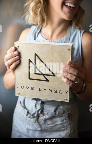 A woman in a blue apron holding her business sign, a square piece of wood with a triangle logo. Stock Photo