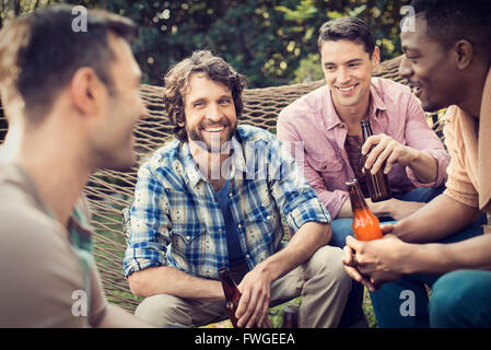 A group of friends lounging in a large hammock in the garden having a beer. Stock Photo