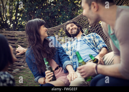 A group of friends lounging in a large hammock in the garden having a beer Stock Photo